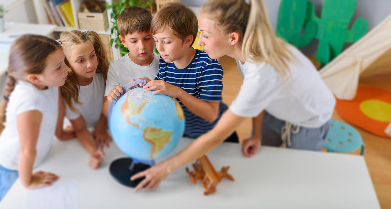 Betreuerin mit Schulkindern, die einen Globus anschauen